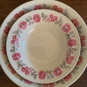 May include: A set of two white ceramic bowls with a floral pattern. The bowls have a pink and grey floral design with a white background.