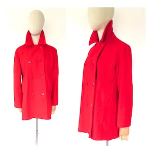 May include: A bright red double-breasted coat with a high collar. The coat has two rows of buttons and a tailored fit. The coat is displayed on a mannequin. The coat is a vibrant shade of red.