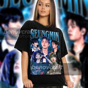 May include: Black t-shirt with a graphic print of a group of men with the word "SEUNGMIN" printed in blue letters.