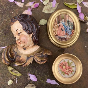 Könnte beinhalten: Drei gerahmte Stücke Nadelmalerei. Das erste ist ein geschnitzter Holzengelkopf mit goldenen Akzenten. Das zweite ist eine Szene mit drei Frauen in einem Raum mit goldenen Verzierungen. Das dritte ist eine einzelne rosa Blume mit grünen Blättern.