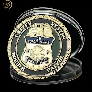 May include: Gold-colored coin with a black and green border patrol badge. The badge features an eagle, the words "CBP Border Patrol", and "U.S. Patrol Agent". The coin is surrounded by a gold-colored rim with the words "United States Border Patrol".