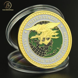 May include: Gold-colored coin with a white and green design. The coin features a stylized eagle with a trident and the words "United States Naval Special Warfare Command".