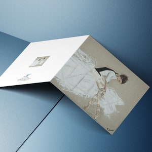May include: A folded card with a white background and a small image of a ballerina on the front. The back of the card features a larger image of a ballerina in a white tutu, with a black bodice, and pointe shoes. The ballerina is sitting on the floor with her legs extended.