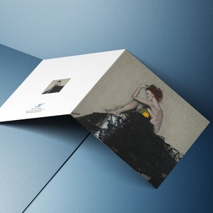 May include: A woman with red hair sits on a black fabric with a yellow flower. The image is printed on a white card with a smaller image of the woman in the corner.