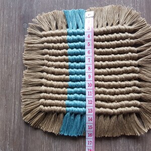 May include: A square woven coaster with a blue and brown colour scheme. The coaster is approximately 15 cm wide and has a fringe border.