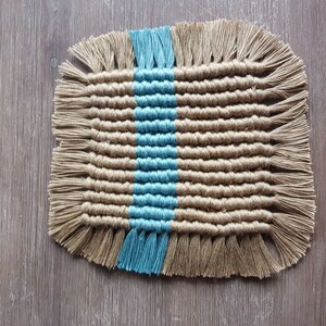 May include: A woven coaster with a blue and brown striped pattern. The coaster has fringe around the edges.
