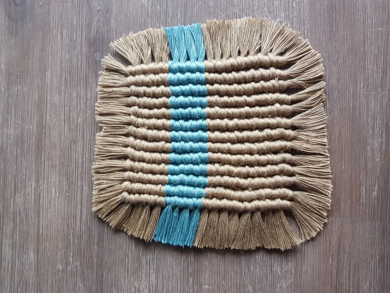 May include: A woven coaster with a blue and brown striped pattern. The coaster has fringe around the edges.