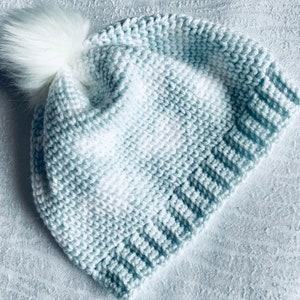 May include: A light blue crocheted beanie with a white pom pom on top. The beanie has a gradient pattern of light blue and white.