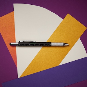 May include: A black and silver multi-tool pen with a ruler on a purple, orange, and yellow background.
