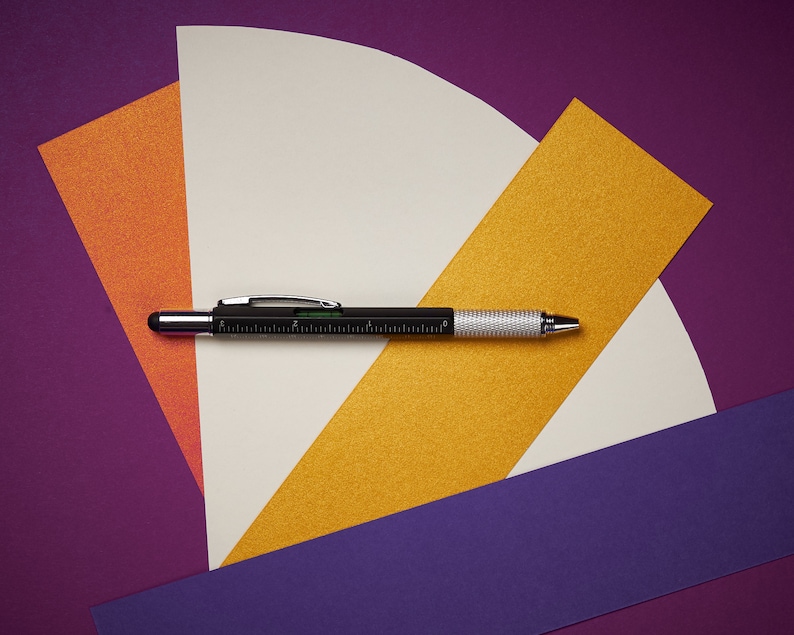 May include: A black and silver multi-tool pen with a ruler on a purple, orange, and yellow background.