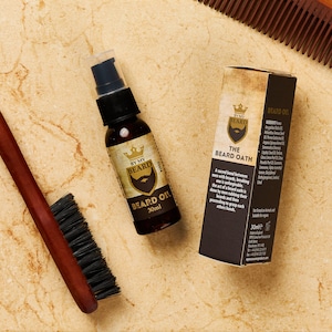 May include: A brown wooden comb, a brown wooden brush, and a glass bottle of beard oil with a gold label that says "By My Beard The Beard Oath" and "Beard Oil 30ml".