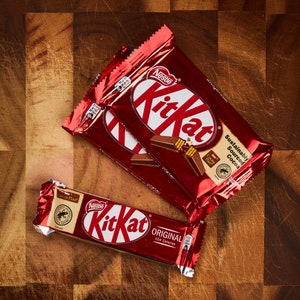 K&ouml;nnte beinhalten: Zwei rote und wei&szlig;e Kit Kat Schokoladenriegelverpackungen mit dem Text "Nestle Kit Kat" und "Nachhaltig Bezogener Kakao". Eine kleinere rote und wei&szlig;e Kit Kat Verpackung mit dem Text "Original 164 Kalorien" befindet sich im Vordergrund.