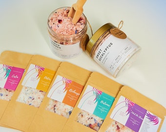 Può includere: Due barattoli trasparenti riempiti di sali da bagno, etichettati Lemon Ginger e Sweet Eucalyptus, con un cucchiaio di legno. Cinque buste di carta marrone con finestre trasparenti contengono sali da bagno etichettati Calm, Detox, Recharge, Balance e Total De-Stress.