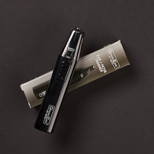 May include: Black electric ear and nose trimmer with a silver label that reads "Groom Ease by Wahl" and "Ear + Nose Trimmer". The trimmer is on a black surface.