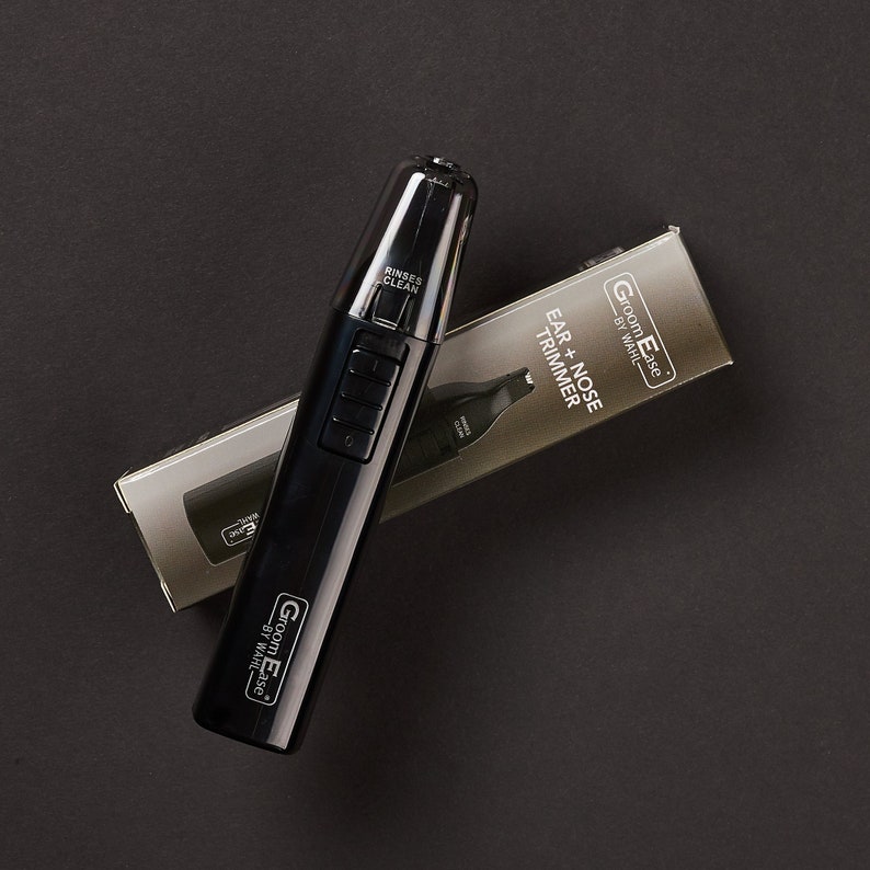 May include: Black electric ear and nose trimmer with a silver label that reads "Groom Ease by Wahl" and "Ear + Nose Trimmer". The trimmer is on a black surface.