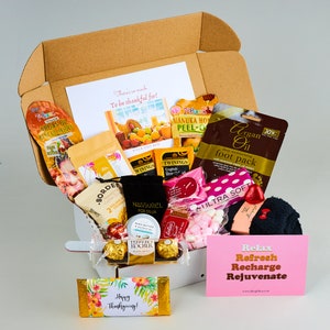 May include: A packed gift box containing a variety of treats such as Argan Oil foot pack, tea bags, chocolates, and a chocolate bar with "Happy Thanksgiving!" on it. A pink card says "Relax, Refresh, Recharge, Rejuvenate."