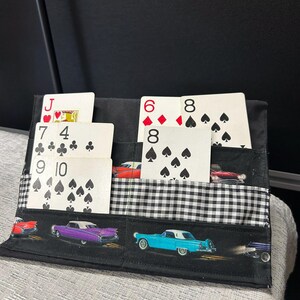 Peut inclure: Porte-cartes en tissu noir avec des poches contenant des cartes à jouer. Le support présente un motif à carreaux noir et blanc et un motif de voitures anciennes. Les cartes visibles incluent un Valet de Coeur, un 7 de Trèfle et un 6 de Carreau.