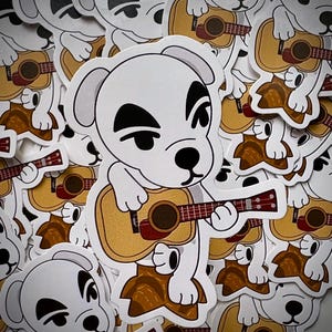 以下が含まれることがあります： 茶色とベージュのウクレレを演奏する犬の白いステッカー。ステッカーには白い縁があります。ステッカーは、ビデオゲームAnimal Crossingのファン向けである可能性があります。