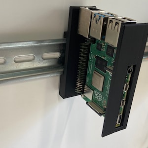Könnte beinhalten: Ein schwarzes 3D-gedrucktes Gehäuse für einen Raspberry Pi-Computer, montiert auf einem Metallgestell. Das Gehäuse hat Ausschnitte für die Anschlüsse des Raspberry Pi, darunter USB, HDMI und Ethernet.