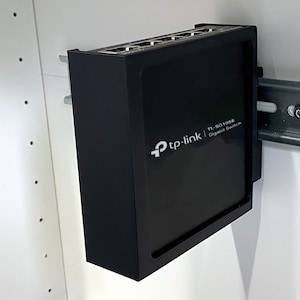 May include: A black TP-Link TL-SG105E Gigabit Switch mounted on a metal rack. The switch has five ports and is labeled with the TP-Link logo and product information.