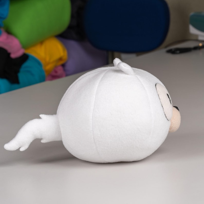 May include: White plush toy shaped like a round, cartoon character with a long, curled tail. The toy has black eyes and a black nose.