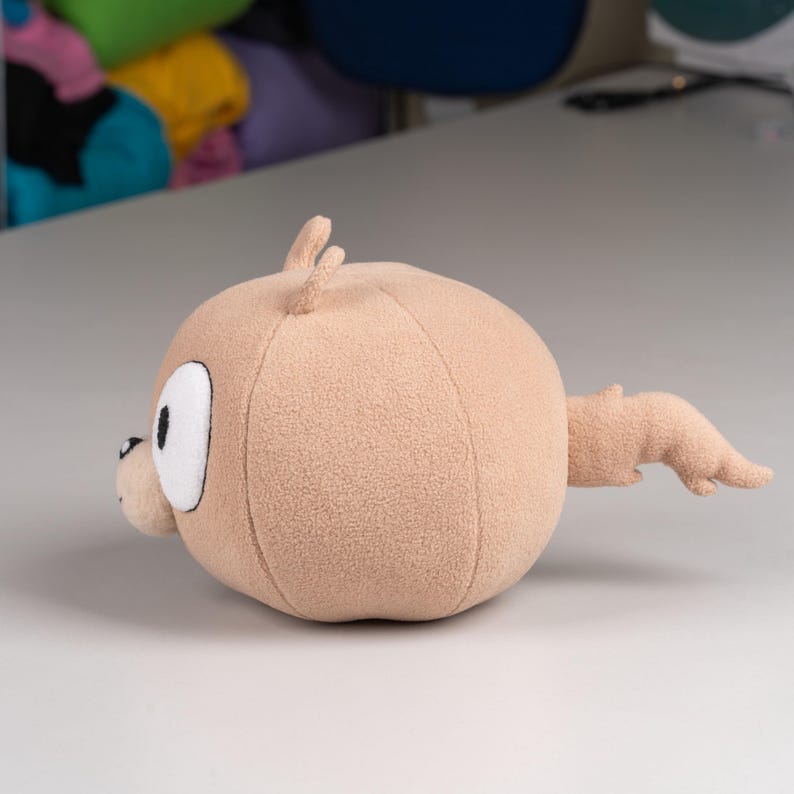 May include: A plush toy shaped like a brown squirrel with a large head and a small tail. The toy has a white face with black eyes and a black nose.