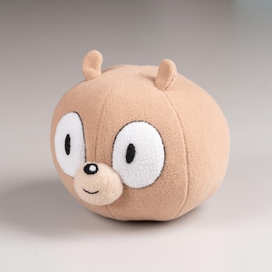 May include: A plush brown bear with large white eyes and a black nose. The bear has a simple, cartoon-like design.