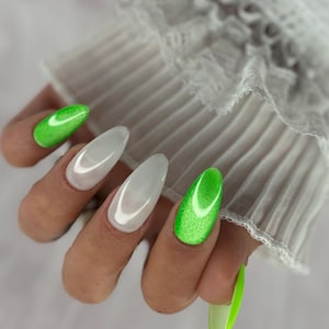 Könnte beinhalten: Mandelformige Nägel mit leuchtend neongrünem Katzenaugen-Nagellack auf Daumen und Ringfinger, während Zeige- und Mittelfinger ein glattes, milchig-weißes Finish aufweisen. Die Nägel sind lang und manikürt mit einer glänzenden, reflektierenden Oberfläche.