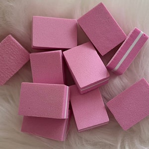 Könnte beinhalten: Ein Satz rosa Nagelpuffer mit weißen Kanten. Die Puffer sind rechteckig und haben eine strukturierte Oberfläche.