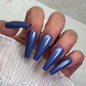May include: Close-up of a hand with long, blue, shimmery, coffin-shaped nails.