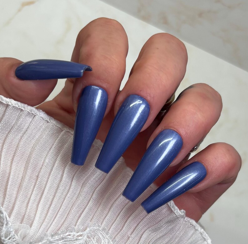 May include: Close-up of a hand with long, blue, shimmery, coffin-shaped nails.