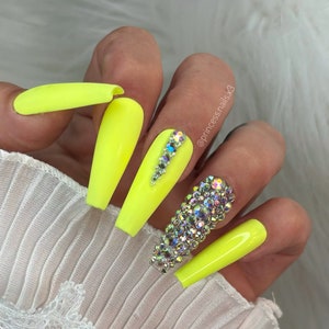 Könnte beinhalten: Neon gelbe lange Press-on-Nägel mit einer Reihe von Strasssteinen auf einem Nagel und einem einzelnen Strassstein auf einem anderen Nagel.  @princessnailsx3