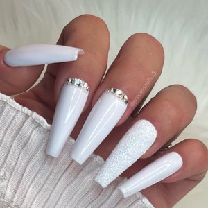 May include: White long, coffin-shaped acrylic nails with a sparkly glitter accent nail. Some nails have a row of rhinestones at the base.