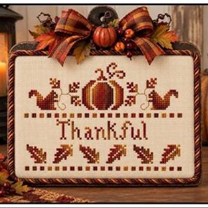May include: A cross-stitch pattern titled Thankful by Plum Pudding NeedleArt. The design features a central pumpkin, two squirrels, and autumn leaves in shades of orange, brown, and red on cream fabric. It includes a plaid bow and berries.
