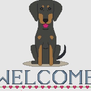 May include: A cross-stitch design featuring a seated black and tan dog with a pink tongue. Below the dog, the word "WELCOME" is stitched in blue, with a row of pink hearts underneath. The design is on a white background.