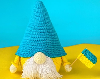 May include: A crocheted gnome with a blue hat and yellow beard holding a small yellow and blue flag. The gnome is sitting on a yellow surface.