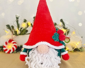 May include: A handmade Christmas gnome with a red conical hat, white beard, and a pink nose. The gnome wears a green jacket with red mittens. The hat is trimmed with white and decorated with green leaves and red berries. A festive holiday decoration.