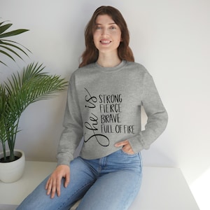 May include: Gray sweatshirt with the text "She is strong fierce brave full of fire" printed on the front.