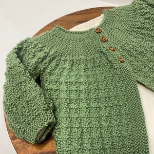 Puede incluir: Un suéter de punto verde para bebé con botones de madera.