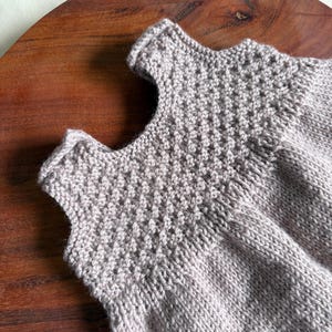 K&ouml;nnte beinhalten: Nahaufnahme eines hellgrauen Stricktops. Das Oberteil hat ein strukturiertes, gemustertes Joch und ein schlichtes, &auml;rmelloses Design. Das Kleidungsst&uuml;ck ist aus weichem Garn gefertigt und scheint handgefertigt zu sein.