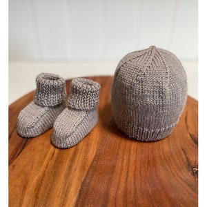 May include: A set of gray knitted baby booties and a matching hat. The booties have a fold-over cuff and the hat is a simple beanie style.