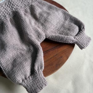 K&ouml;nnte beinhalten: Ein helllila Strickpullover mit strukturiertem Joch und gerippten B&uuml;ndchen. Der Pullover hat lange &Auml;rmel und wird auf einer Holzoberfl&auml;che pr&auml;sentiert. Das Kleidungsst&uuml;ck ist aus einem weichen, m&ouml;glicherweise wollenen Material gefertigt.