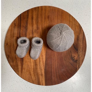 May include: A set of knitted baby booties and a matching hat in a light gray color. The items are displayed on a wooden surface.