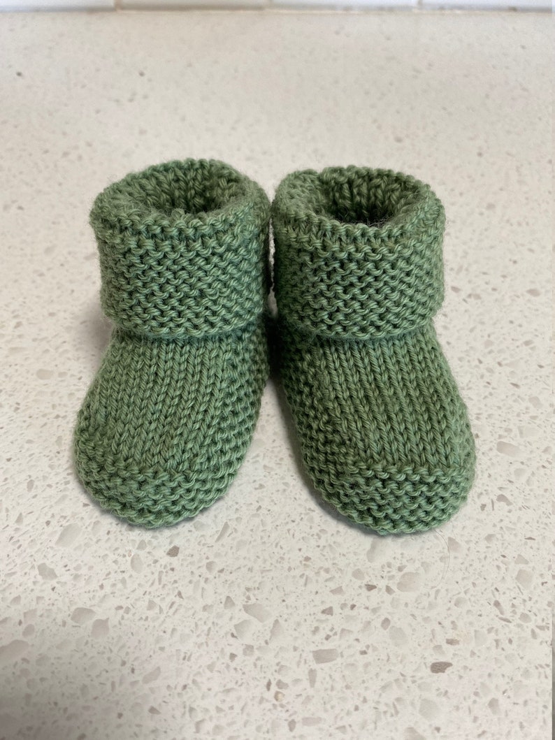 May include: A pair of green knitted baby booties with a folded cuff.