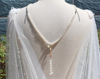 May include: A white tulle bridal cape with pearl embellishments and a pearl and gold chain necklace.