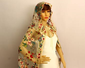 Pode incluir: Uma capa de noiva transparente creme com bordados florais em vermelho, rosa, verde e azul. A capa apresenta um capuz e drapeja sobre os ombros, criando um visual romântico e elegante. O design floral é concentrado ao longo das bordas e do capuz.
