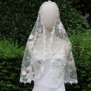 May include: A white lace veil with floral embroidery in shades of pink and green. The veil is delicate and sheer, with a scalloped edge.
