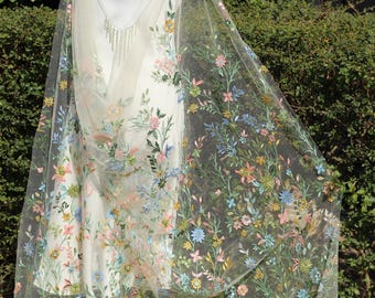 May include: A sheer white shawl with delicate floral embroidery in shades of pink, blue, and green. The embroidery features a variety of flowers and leaves, creating a romantic and whimsical design.