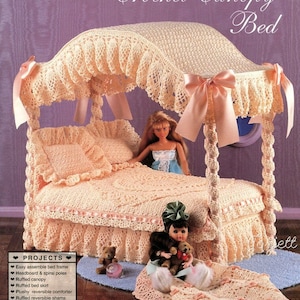 Puede incluir: Cama con dosel de crochet para muñecas, con un dosel de crochet blanco, una colcha de crochet rosa y blanco y una falda de crochet blanca. La cama está decorada con cintas rosas y una muñeca está sentada en la cama. El texto "Crochet Canopy Bed" está impreso en la imagen.