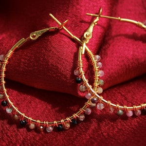 Peut inclure: Une paire de cr&eacute;oles dor&eacute;es avec un fil m&eacute;tallique enroul&eacute; le long des anneaux. De petites perles facett&eacute;es multicolores dans des tons de rose, noir et blanc translucide sont fix&eacute;es &agrave; intervalles r&eacute;guliers sur toute la circonf&eacute;rence.